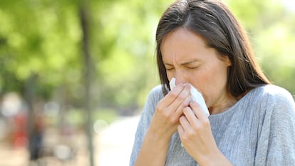 Una mujer estornuda en un parque a causa del polen.