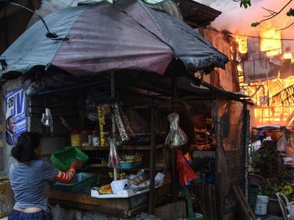 Una vendedora recoge sus bienes de un puesto próximo a una casa en llamas tras un incendio en el suburbio de Quezon (Manila). 