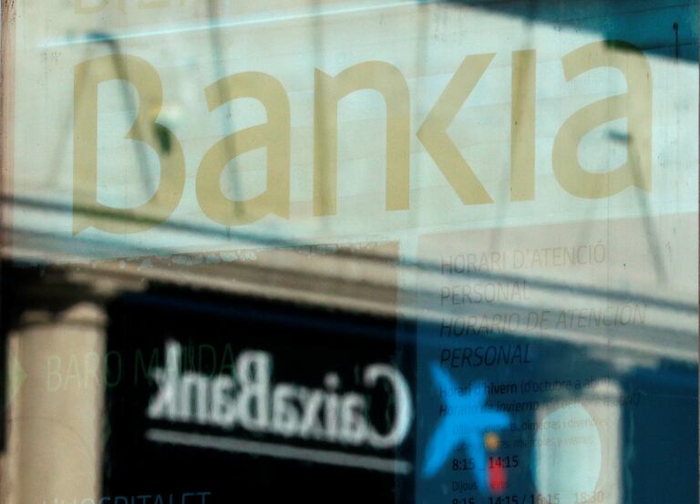 El logo de CaixaBank y el de Bankia se reflejan en el cristal de una sucursal de Barcelona. REUTERS/ Albert Gea