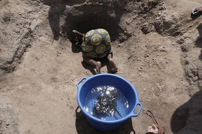 Los pozos de agua son agujeros que han excavado mujeres y niños para encontrar agua cerca de un lago. Una mujer de edad avanzada se agacha para sacar un pequeño balde con agua. 