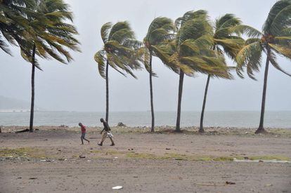 Dos personas caminan bajo el viento y la lluvia por una playa de Cabo Haitiano (Haití).