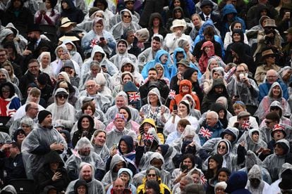 El público congregado para ver parte del recorrido de la llamada procesión del rey —que llevará a Carlos III y Camila de Buckingham a Westminster— se protege de la lluvia con chubasqueros. 