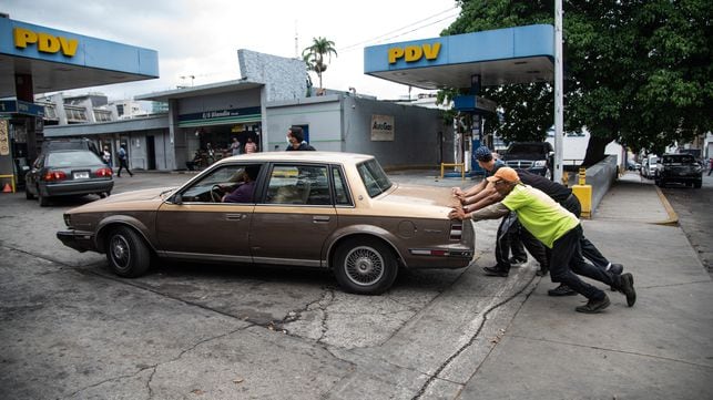 Unos hombres empujan un coche a la entrada de una gasolinera, en junio, en Caracas.