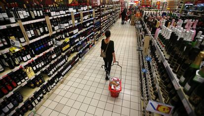 Una mujer con su cesta en la sección de vinos de un hipermercado.