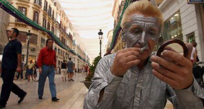 Un mimo se maquilla para actuar en la calle Larios de Málaga.