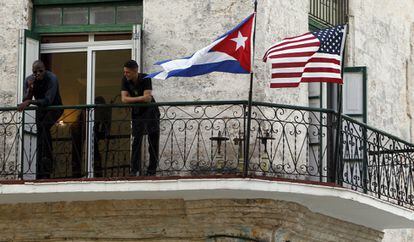 Dos jóvenes cubanos conversan junto a las banderas de Estados Unidos y Cuba, en La Habana