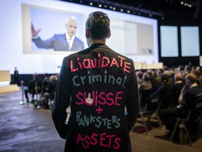 Un hombre viste un traje con la leyenda "Liquidate Criminal Suisse + Banksters Assets", mientras el presidente del banco suizo, Axel P. Lehmann, habla durante la junta anual de accionistas del grupo.