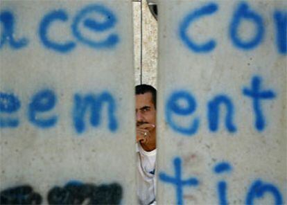 Un palestino mira a través de una brecha en el <i>muro de la vergüenza</i> a su paso por Jerusalén.