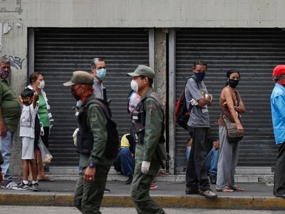 Personas con mascarillas observan a unos agentes de la policía en Caracas, Venezuela.