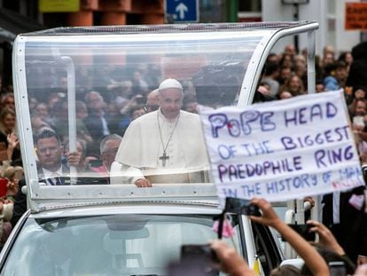 Un activista muestra una pancarta en contra del papa Francisco (c), mientras recorre las calles del centro de Dublín a bordo del papamóvil, ayer. En vídeo: El Papa reza en Dublín por las víctimas de los abusos.