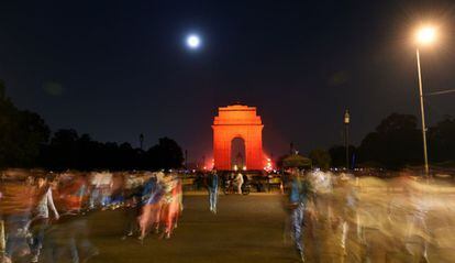 Peatones pasan frente al monumento Puerta de India, en Nueva Delhi, iluminada de color naranja con motivo del Día Internacional de la Eliminación de la Violencia contra la Mujer.