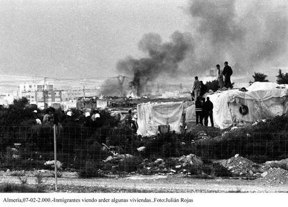 Un grupo de inmigrantes magreb&iacute;es observa c&oacute;mo arden algunas chabolas en El Ejido (Almer&iacute;a), en 2000.