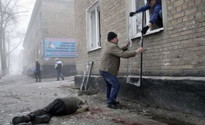 Dos hombres retiran una ventana rota junto a un cad&aacute;ver tras un bombardeo, este viernes en Donetsk. 