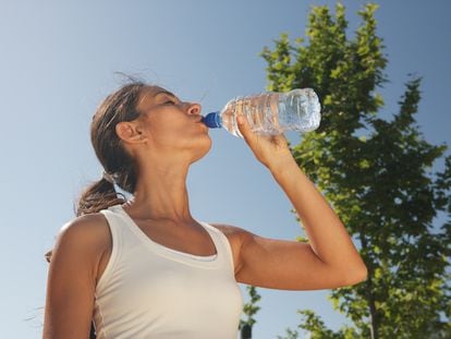 Una mujer bebe de una botella de agua de plástico.