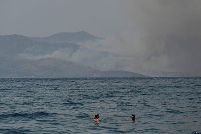 Unos bañistas nadan cerca de la ciudad costera de Saranda mientras el humo se extiende en la isla griega de Corfú.