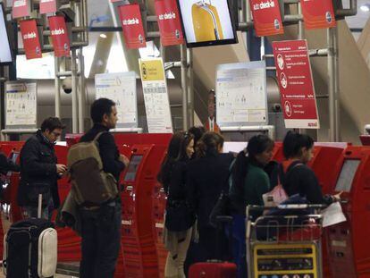 Varias personas guardan cola junto a los mostradores de facturaci&oacute;n de la Terminal T4 del aeropuerto de Madrid-Barajas. 