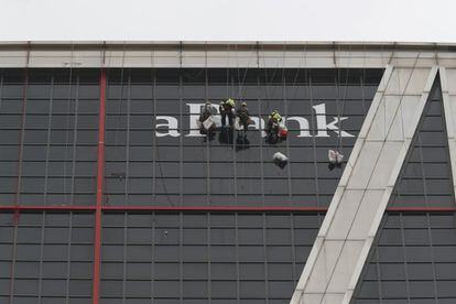 Unos operarios colocan los vinilos con el logo de Caixabank en la parte de atras del edificio.