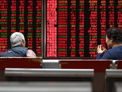 Dos mujeres están sentadas frente a paneles de cotización de valores en Pekín. 