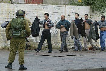 Un grupo de palestinos se levanta la ropa ante la mirada de un soldado israelí en el paso fronterizo de Erez, en la franja de Gaza.
