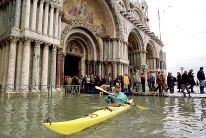 Los turistas salen de la catedral de San Marcos de Venecia, a través de una pasarela, debido al agua que inunda la plaza debido a las fuertes lluvias, mientras un hombre navega en kayak.