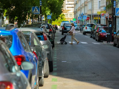 Una mujer cruza una calle en Madrid con vehículos aparcados en la zona de estacionamiento regulado.