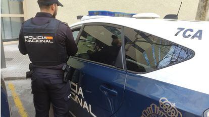 Un agente de la Policía Nacional de espaldas, junto a un coche patrulla.