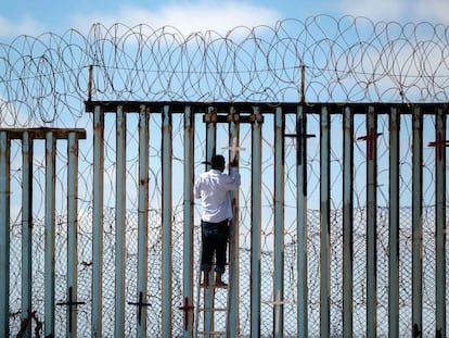 Josue Serrano, un mexicano deportado de EE UU, coloca una cruz sobre el muro fronterizo en Tijuana.