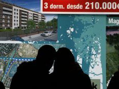 Dos personas observan una oferta de viviendas en uno de los expositores del Sal&oacute;n Inmobiliario de Madrid, SIMA Oto&ntilde;o.