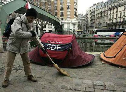 Un indigente barre la acera junto al campamento que Los Hijos de Don Quijote han instalado en el canal Saint Martin en París.
