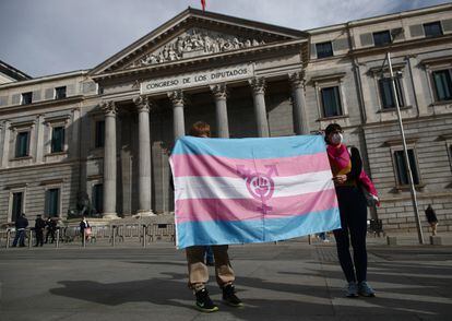 Dos personas sostienen una bandera 'trans' frente al Congreso de los Diputados.