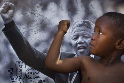 Un niño posa junto a un retrato de Nelson Mandela en el exterior del  Mediclinic Heart Hospital donde se encuentra ingresado desde el pasado 8 de junio debido a un empeoramiento de la infección pulmonar que padece, 14 de julio de 2013. El expresidente de Sudáfrica cumple 95 años.