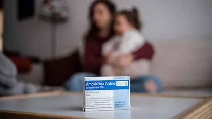 Una caja de amoxicilina en primer término, con una madre y su hija al fondo.