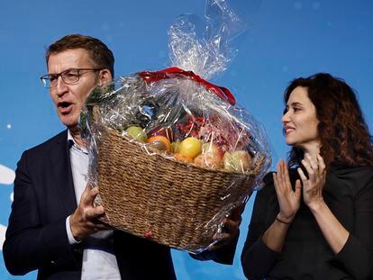 El presidente del PP, Alberto Núñez Feijóo, sostiene una cesta de fruta junto a la presidenta de la Comunidad de Madrid, Isabel Díaz Ayuso, durante la cena de Navidad del PP de Madrid, celebrada este lunes.