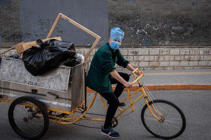 Un trabajador con mascarilla lleva un cargamento de basura en su triciclo.