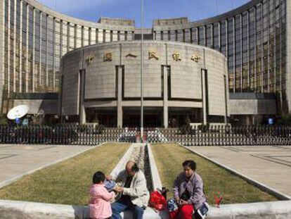 Una familia descansa delante de la sede del Banco Popular de China en Pek&iacute;n (China). 