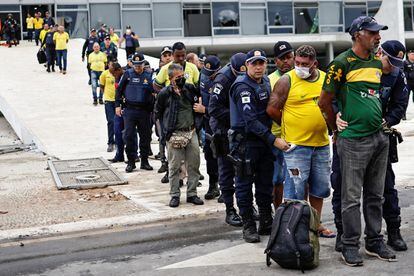Bolsonaristas detidos em flagrante pela polícia, alinhados em frente ao Planalto.