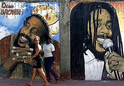 Dos jamaicanas pasan delante de un mural que representa a los músicos de <i>reggae</i> Denis Brown y Bob Marley en la capital, Kingston, adonde llegaron ayer Isabel II de Inglaterra y su esposo.