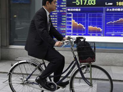Un hombre pasa en bicicleta por delante de una pantalla con los datos de la bolsa de Tokio (Jap&oacute;n).