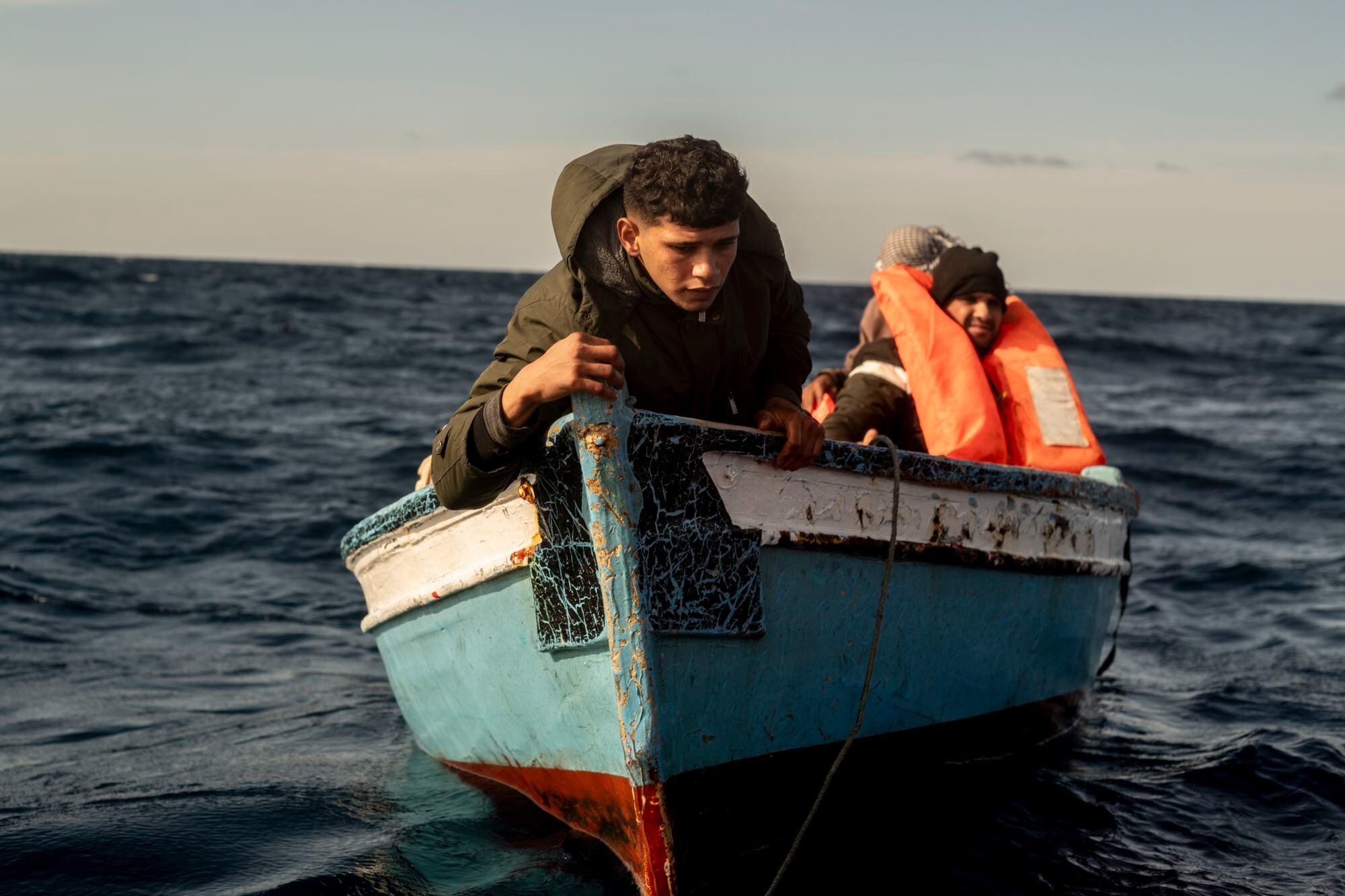 Un joven, a la deriva en un pequeño bote de madera junto a cinco compañeros de viaje, intenta recuperar un chaleco salvavidas arrojado por la tripulación de la lancha de rescate mientras lo trasladan al barco de Open Arms.
