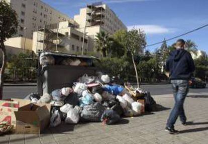 Un hombre pasa ante contenedor repleto frente al Hospital General de Alicante dónde se mezclan la basura de los ciudadanos con los residuos que genera el centro hospitalario en la quinta jornada de huelga de la empresa del servicio de recogida.