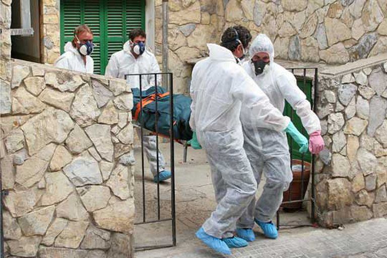 Trabajadores de una empresa funeraria de Palma trasladan un cadáver equipados con monos y mascarillas.