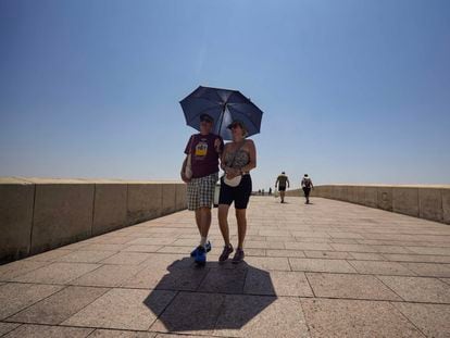 Una pareja de turistas caminan bajo un paraguas para paliar los rayos de sol, este lunes por el Puente Romano de Córdoba.