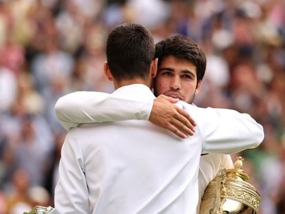 Carlos Alcaraz sujetando el trofeo de Wimbledon mientras abraza a Novak Djokovic.