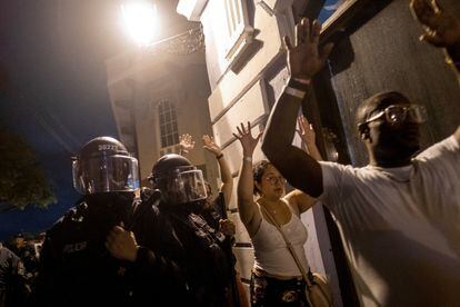 Dos turistas levantan las manos mientras caminan junto a  policías antidisturbios de Puerto Rico durante los enfrentamientos de este jueves.