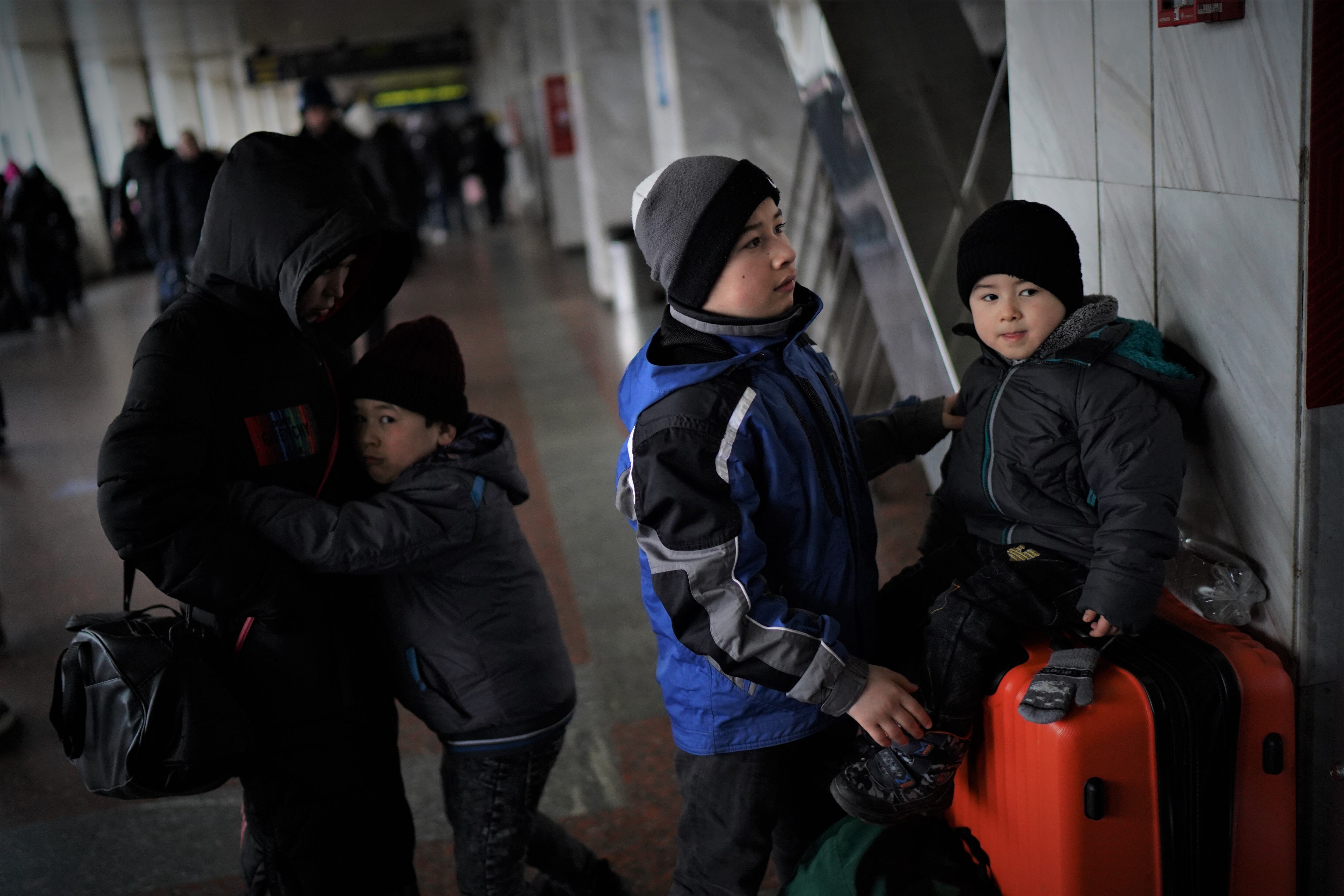 Islam, 12, en el centro, cuida de su hermano Yasín, 4, mientras otro hermano, Illias, de siete, se abraza a su madre, en la estación de Kiev.