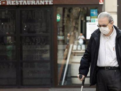 Una persona mayor protegida con mascarilla arrastra un carro frente a un comercio cerrado, en Valencia.