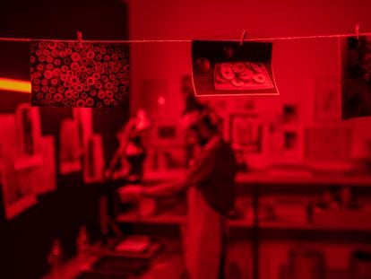 Row of several wet developed photos hanging on thread against young modern photographer working in red lit laboratory