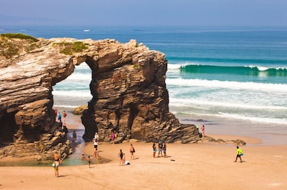 Entre paseo costero y visita monumental (casi nadie se baña en este arenal gallego), así se concibe la playa de As Catedrais o Augas Santas, accesible solo en marea baja, único horario que permite el Cantábrico escudriñar este portento de la Mariña lucense. Uno no sabe qué admirar más en esta catedral marina, si las ocho arcadas pizarrosas que quieren ser arquivoltas góticas —las más bellas están casi metidas entre las olas—; si la espaciosidad de las cuevas; si el imponente arco que nos recibe a la entrada (y que amenaza ruina según los geólogos), o tal vez los entresijos que forma el mar al roer la base de los cantiles. Del 1 de julio al 30 de septiembre el acceso deja de ser libre y se precisa una autorización <a href="https://ascatedrais.xunta.gal/monatr/inicio" target="_blank">(ascatedrais.xunta.gal)</a> para bajar a este monumento natural, salvo que se pernocte en alguno de los alojamientos oficiales de Ribadeo, o se desplace el visitante desde el centro de esta localidad en autobús lanzadera (150 autorizaciones diarias) o con el recibo del taxi. La playa está señalizada en la autovía.