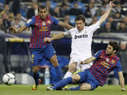 Los azulgrana Dani Alves y Cesc F&agrave;bregas disputan un bal&oacute;n con el jugador del Real Madrid, Xabi Alonso.  
