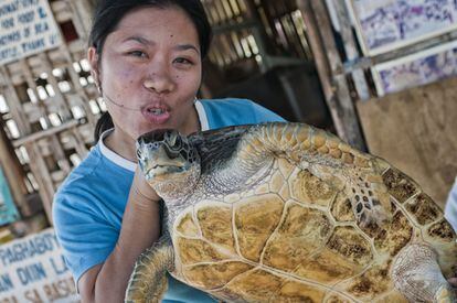 Una turista asiática se fotografía con una tortuga en Filipinas. El animal es agarrado como a la mujer le place, sin que haya sido advertida de la mejor forma de hacerlo. Luego la tortuga será metida en una jaula.